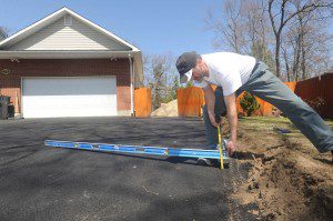 Vladimir Lesnik uses a level to determine that one side of a new driveway installed at his Barbara Street home by an out-of-state contractor is more than four inches lower than the center. (Photo ©2013 Carl E. Hartdegen)  