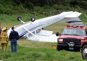 Emergency personnel from the Southwick fire department stand by a small Cessna aircraft that flipped over after an emergency landing in a grass field at 247  North Loomis Street this morning. The pilot escaped with just a small cut on his nose according to witnesses on the scene. (Photo by Frederick Gore) 