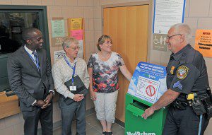 Southwick Police Sergeant Kevin Bishop, right, formally accepts a MedReturn prescription drug return receptacle from, left-right, Soloe Dennis, left, regional director of the Commonwealth of Massachusetts Department of Public Health, Southwick Health Inspector Thomas Fitzgerald, and Southwick Town Nurse Kate Johnson, in the Southwick Police Department lobby yesterday. The receptacle is a secure container that will be used to dispose unwanted prescription medication. (Photo by Frederick Gore)  