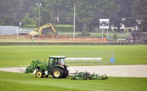 A maintenance worker from the Southwick -Tolland Regional School District cuts the lawn near the softball field as contractors, rear, demolish the former running track near the Powder Mill Middle School Thursday. (Photo by Frederick Gore)