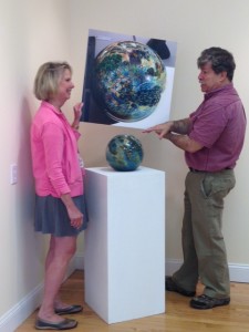 Josh Simpson (right) explains to Faith Lund (left), curator of the WSU Downtown Art Gallery, how a photo of one of his Megaplanets compares to the actual glass sculpture which will be on display at the Westfield State Downtown Art Gallery at 105 Elm Street in Westfield during the Universe According to Josh Simpson. (Photo submitted)