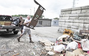 Mike Zajdel, center, throws an old headboard into a scrap pile at the Twiss Street Recycling Center as his dad Dave, rear left, removes debris from the pickup truck yesterday. (Photo by Frederick Gore)