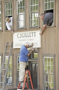 Volunteers William Morrissey, center, of Southwick, uses a bubble level to check the installation of new sign sign at the C. J. Gillett building, as John Bannish, top left, and Mike Morrissey, top right, secure the sign. The Southwick Historic Museum is located at 86-88 College Highway in Southwick. (Photo by Frederick Gore)