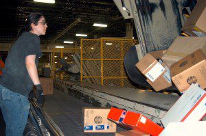 Laura Moodi, a mail handler, helps empty a container of packages on the conveyer belt. (Photo by Jeff Hanouille) 
