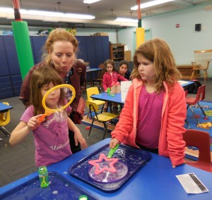 Anne Rock, from the board of the Shurtleff Children’s Services Fund, helps Gianna to blow a bubble from the gravity STEM kit at the Athenaeum, while Jordan waits her turn.