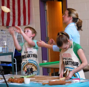 Baking assistant Aidan Layng throws pizza dough while Instructor Amy Driscoll supervises and assistant Paris Reed shapes cinnamon buns at King Arthur Flour Bake for Good program at Russell Elementary on Wednesday. (Photo by Amy Porter)