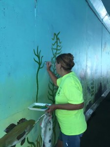 Artist Susan Yates is restoring one of the many fish on the mural. (Photo by Greg Fitzpatrick