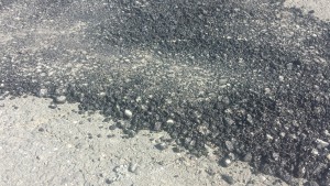 A close-up view of the old style of asphalt repair, with obvious space and loose rock.